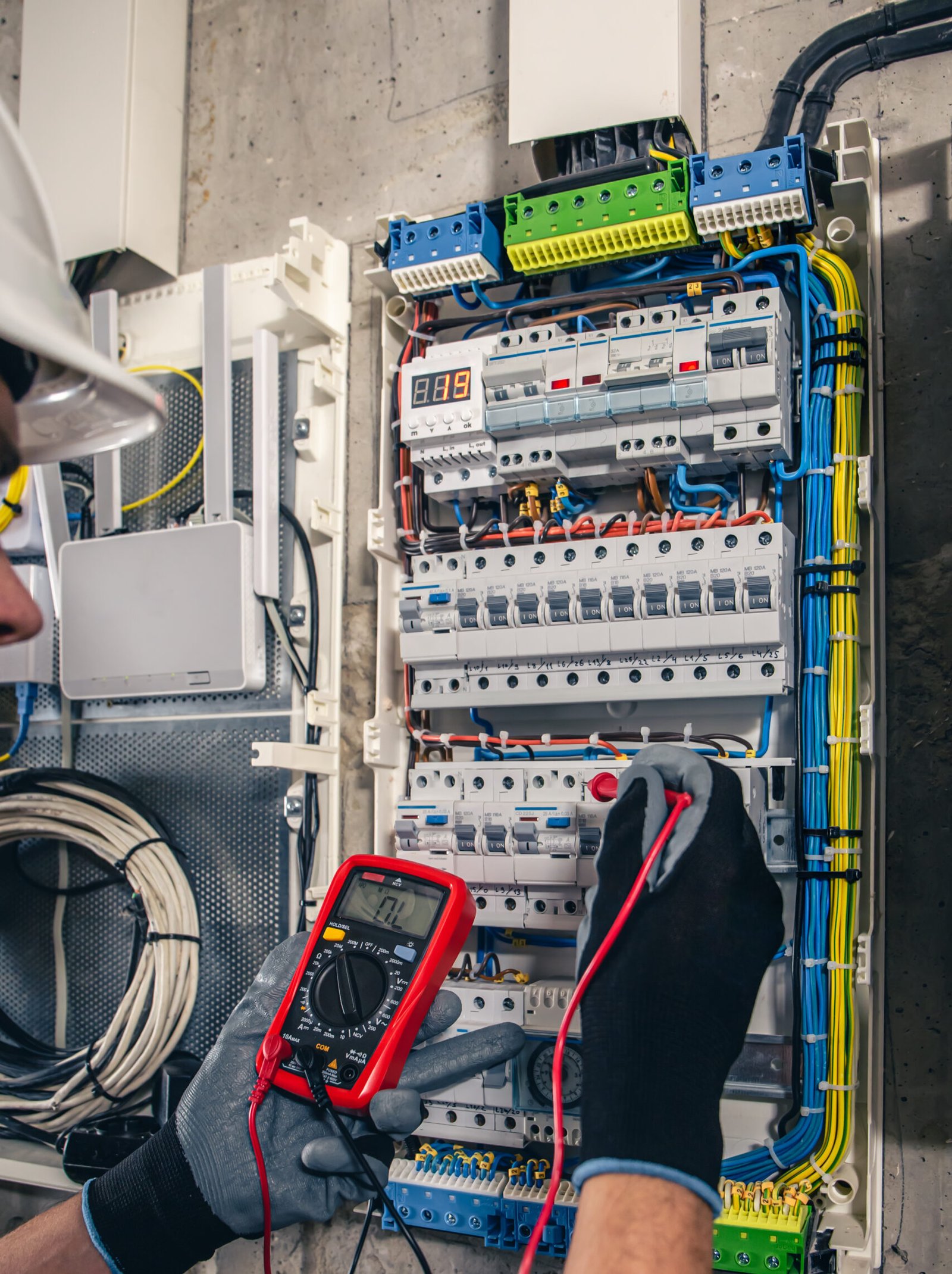 Man, an electrical technician working in a switchboard with fuses. Installation and connection of electrical equipment. Professional uses a tablet.